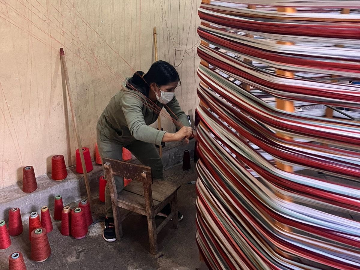 Una artesana amarra hilos rojos en el urdidor de un taller de Peguche