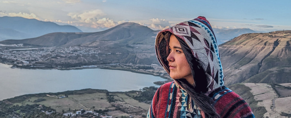 Mujer con el poncho Cayambe y la capucha puesta, frente a una laguna de la sierra