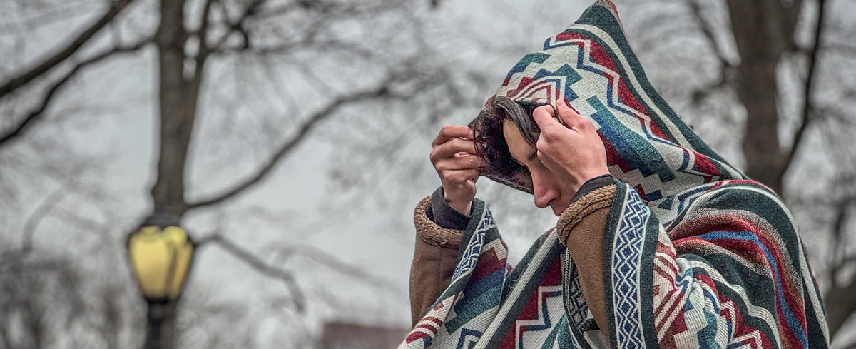 Persona con el poncho Cotopaxi acomodándose la capucha en un parque de Nueva York en invierno