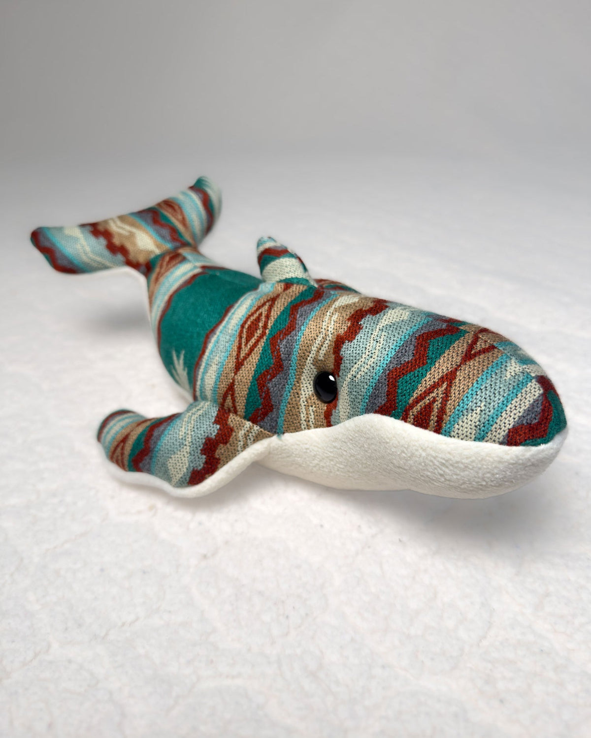 Peluche Wana de ballena jorobada visto de frente, con las aletas abiertas y tela andina de colores