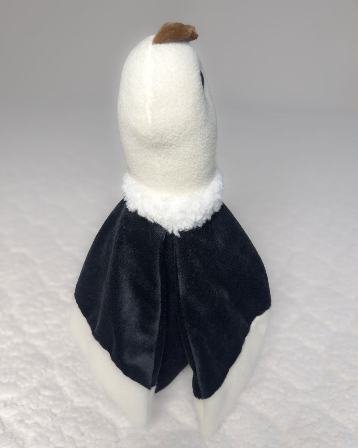 Peluche Kuri de cóndor visto de espaldas, con las alas negras y la cabeza blanca de lado