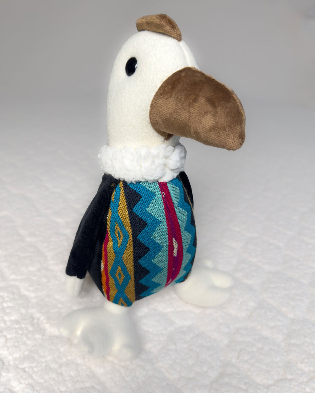 Peluche Kuri de cóndor visto de frente, con el pico café grande, collar blanco y pecho de tela andina