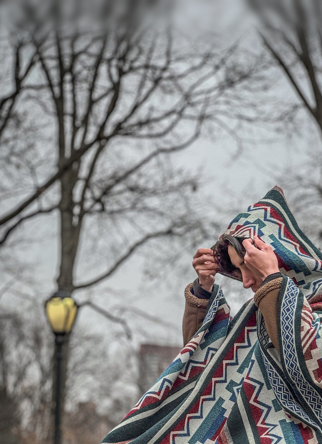 Persona con el poncho Cotopaxi acomodándose la capucha en un parque de Nueva York en invierno