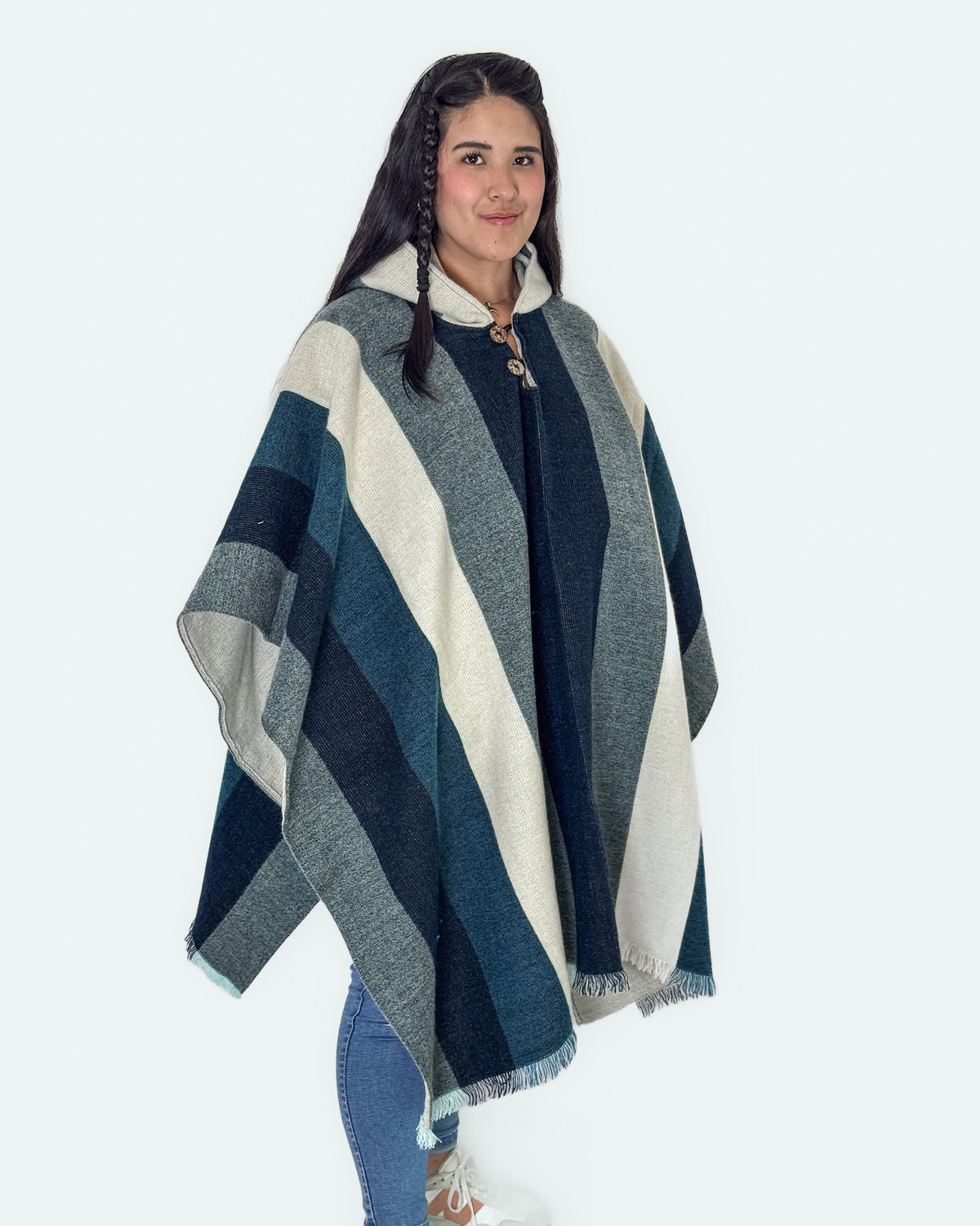 Mujer de tres cuartos con el poncho Cuicocha de franjas azules, grises y crema, con jeans y zapatillas