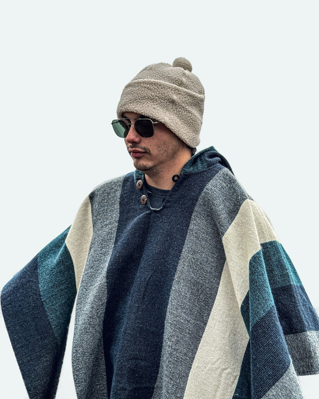 Hombre con gorro de lana y gafas de sol con el poncho Cuicocha de franjas azules, grises y crema