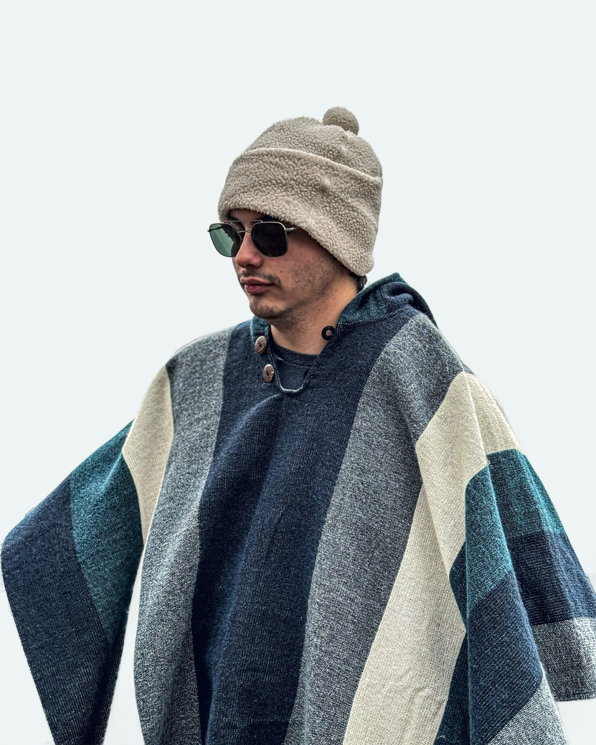 Hombre con gorro de lana y gafas de sol con el poncho Cuicocha de franjas azules, grises y crema