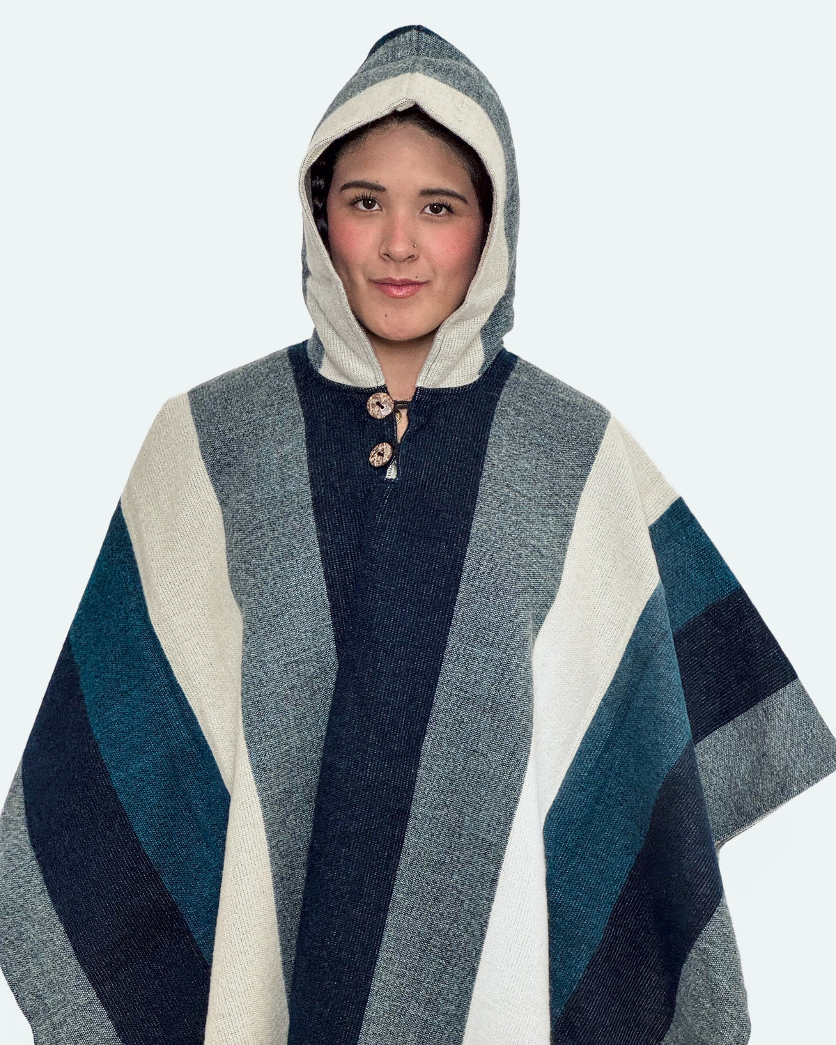 Mujer con la capucha puesta y el poncho Cuicocha de franjas azul marino, gris y crema, con dos botones de coco