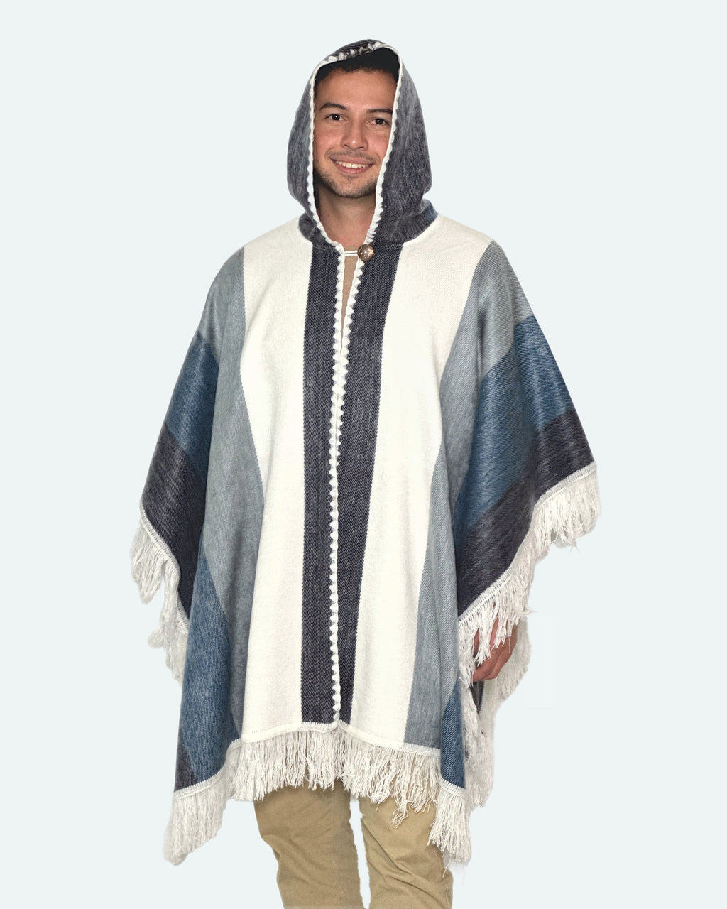 Hombre sonriendo con la capucha puesta y el poncho Espíritu Cielo Andino de franjas azules, grises y blancas