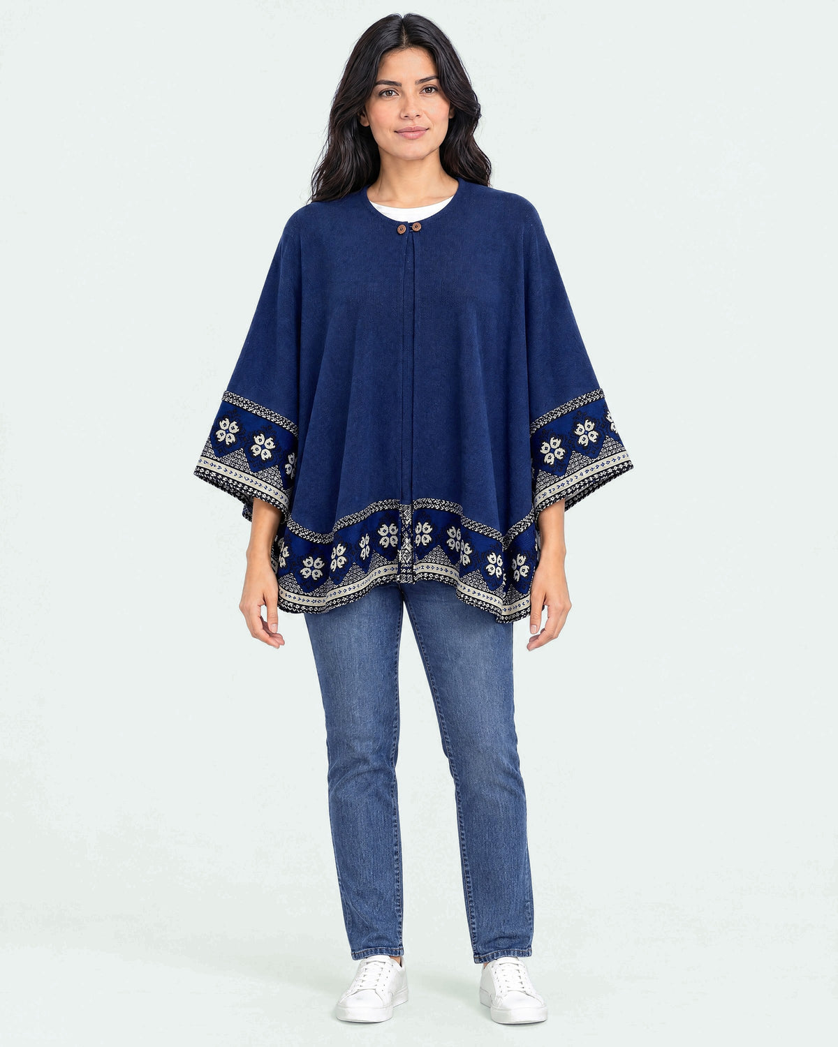 Mujer de cuerpo entero con el Poncho Flor de Imbabura azul y jeans, sobre fondo claro de estudio