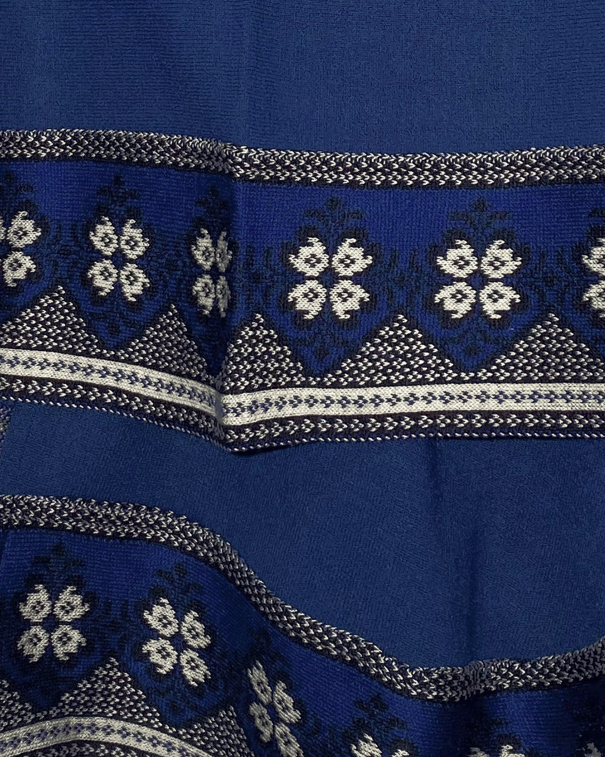 Detalle del tejido con flores blancas y guardas azules en el borde del Poncho Flor de Imbabura