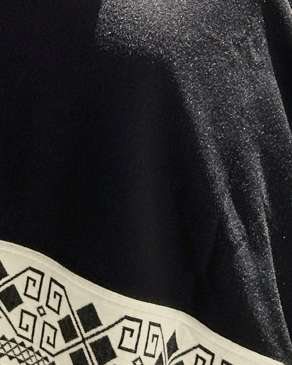 Detalle del tejido negro del poncho Lluvia Nocturna con la greca crema del borde inferior