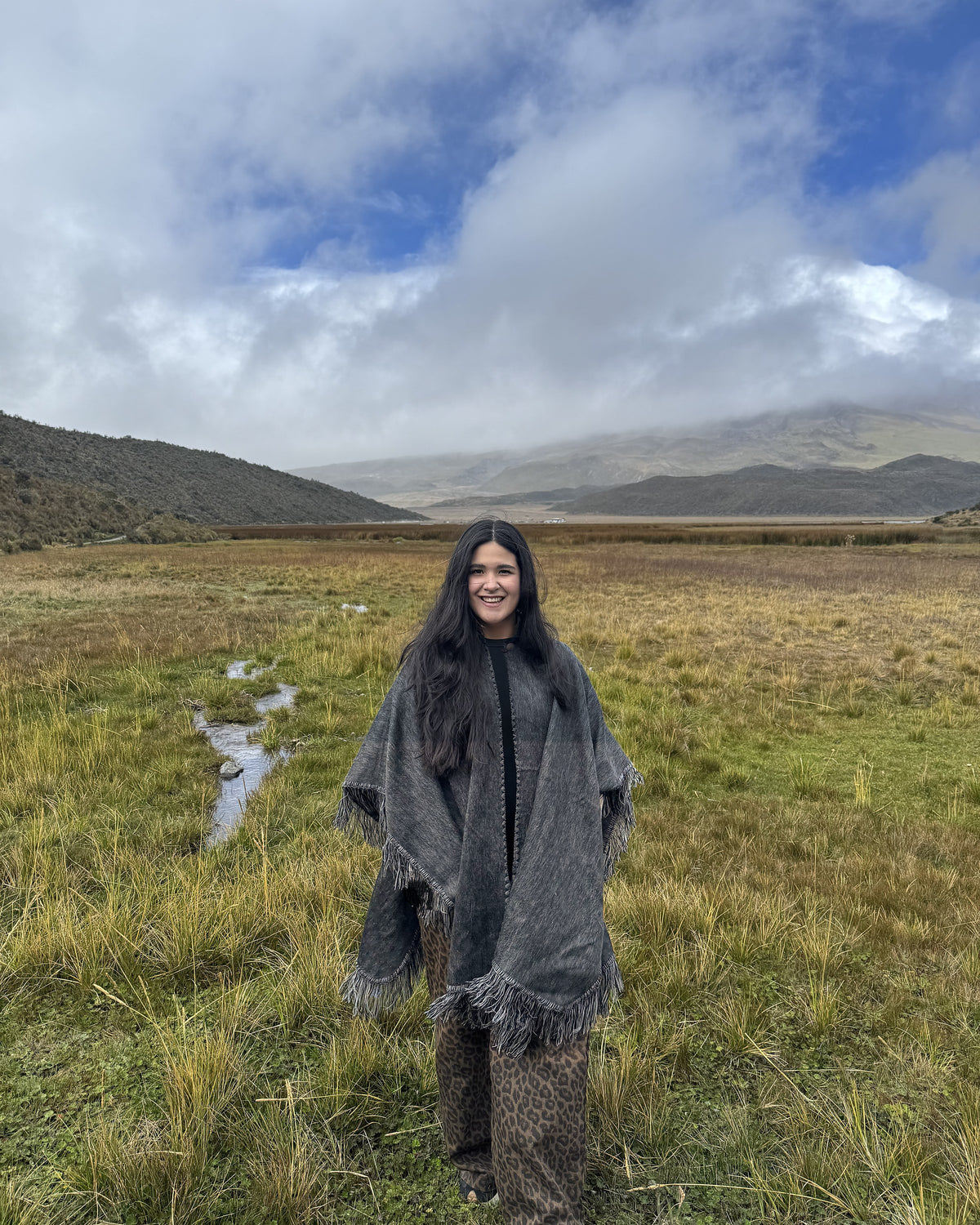 Mujer con el Poncho Sombra Andina gris en un páramo con montañas y cielo nublado