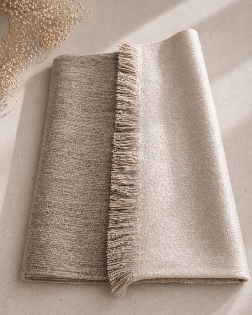 Chal de alpaca doble cara Arena doblado sobre una mesa, beige más profundo de un lado y beige claro del otro
