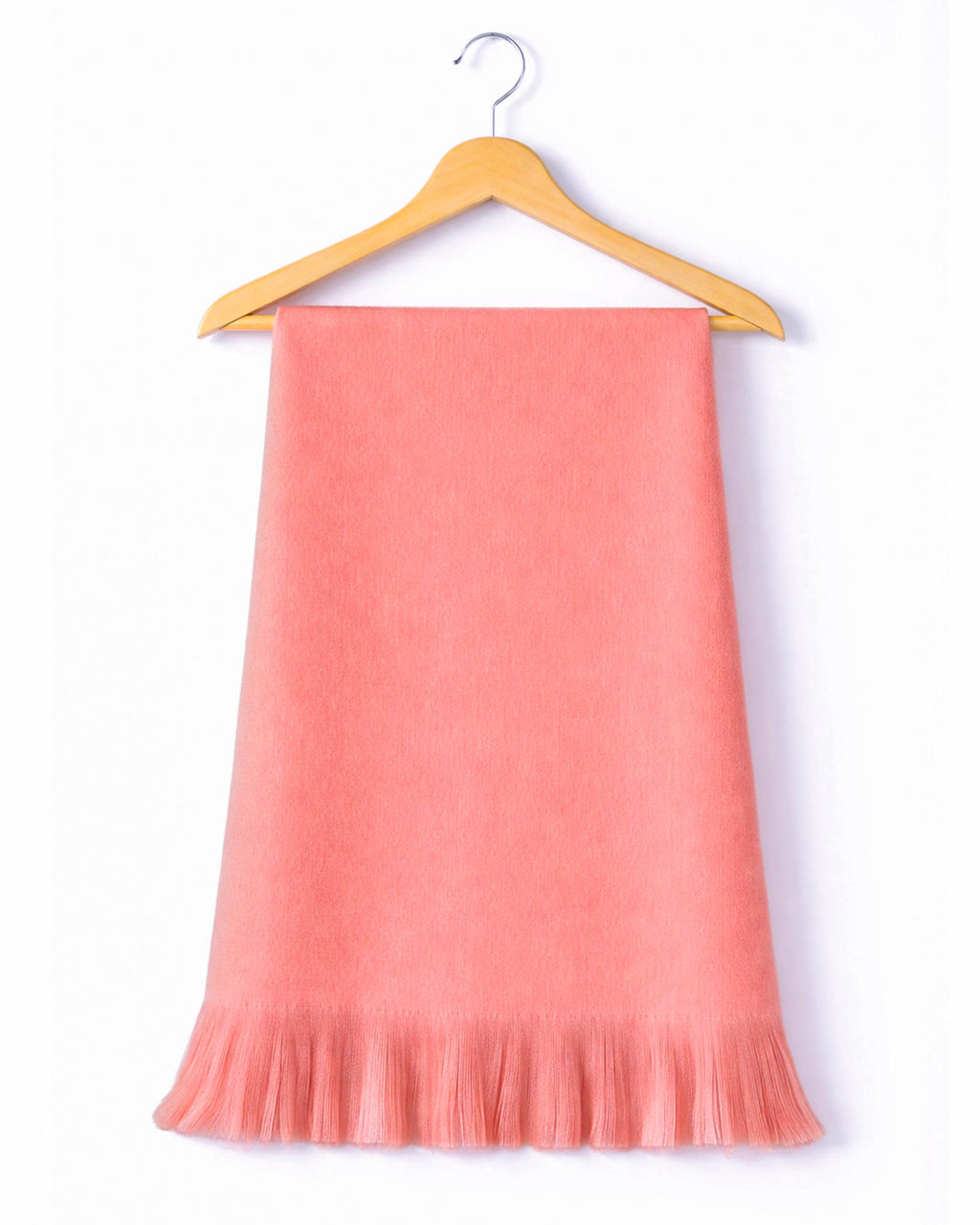 Chal de alpaca Coral Blush con flecos, colgado de una percha de madera sobre fondo blanco
