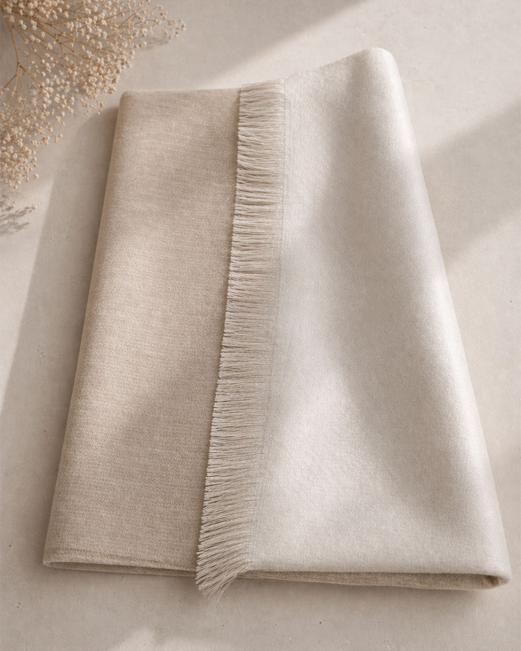 Chal de alpaca doble cara Hueso doblado sobre una mesa, beige cálido de un lado y hueso luminoso del otro