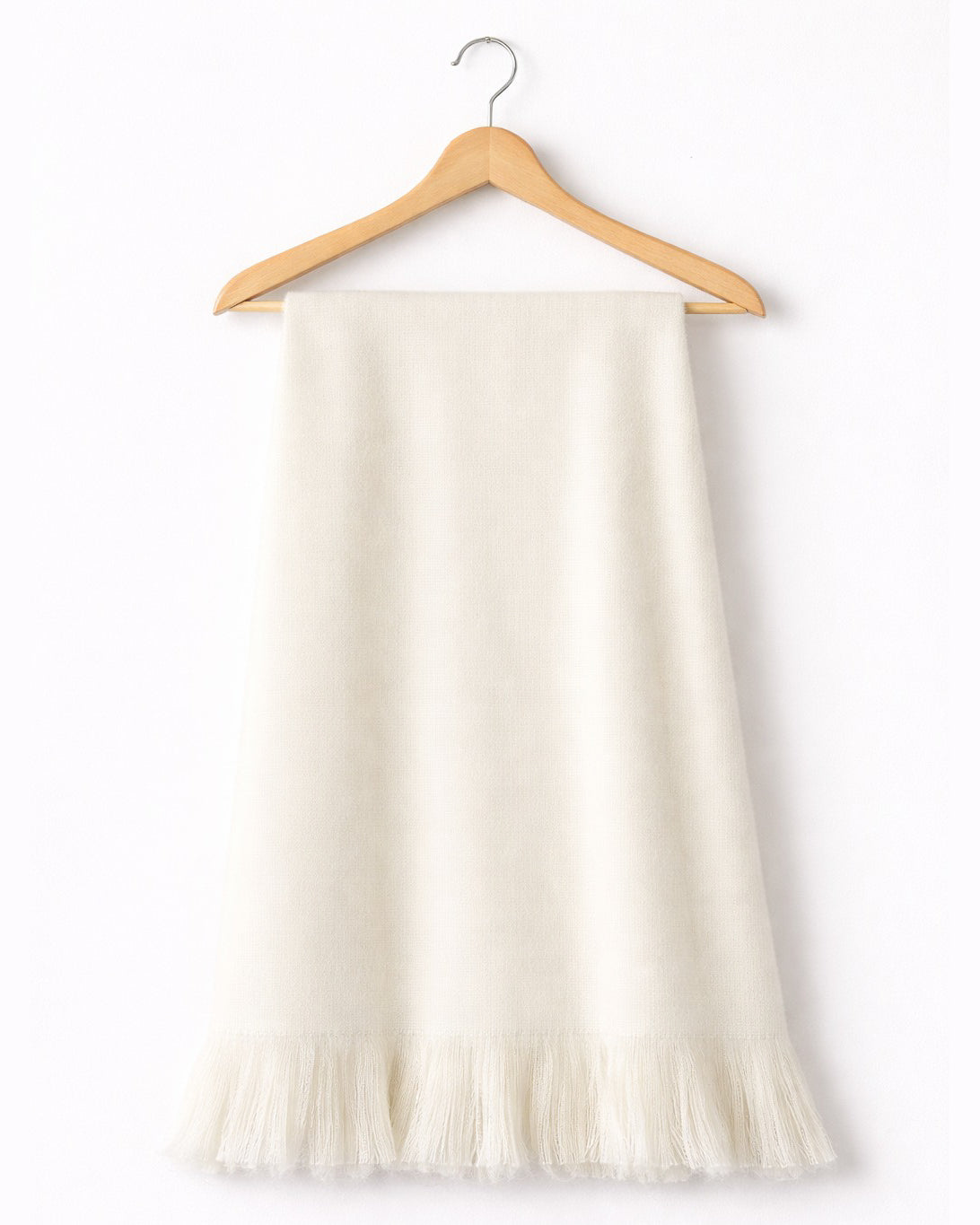 Chal de alpaca Marfil Natural con flecos, colgado de una percha de madera sobre fondo blanco
