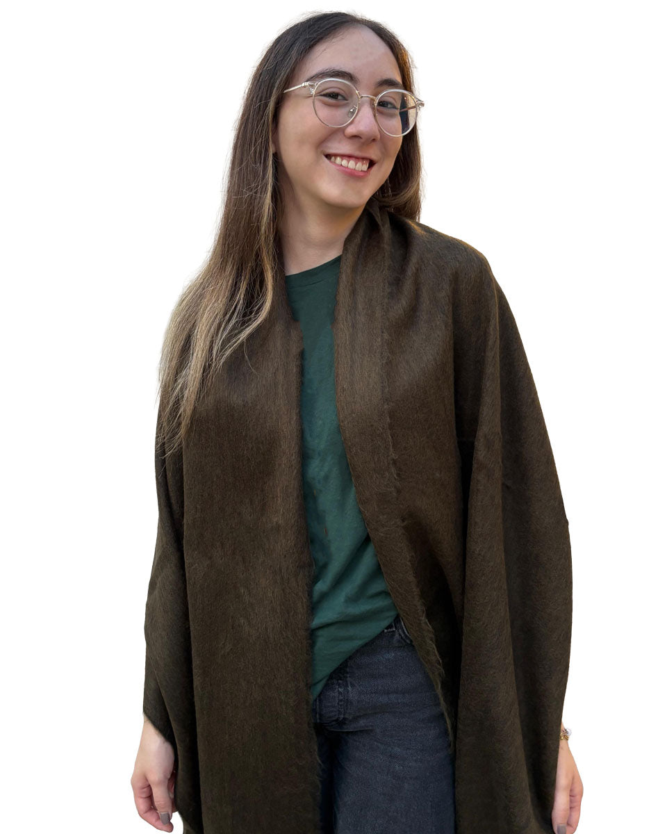 Chal de alpaca Oliva Profundo cubriendo los hombros de una modelo con lentes, en primer plano