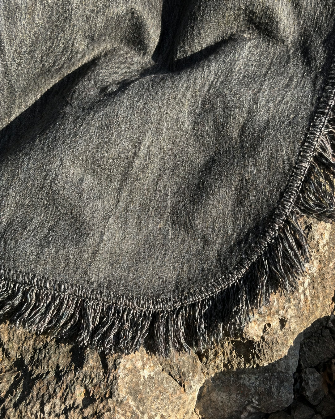 Detalle del borde curvo con flecos del Poncho Sombra Andina gris sobre una roca