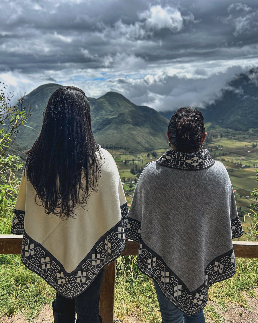 Dos personas de espaldas con ponchos cortos frente al cráter del Pululahua