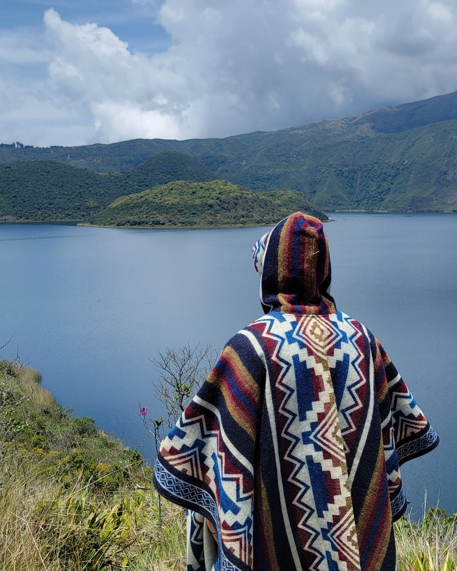 De espaldas con un poncho de capucha frente a las islas de la laguna de Cuicocha