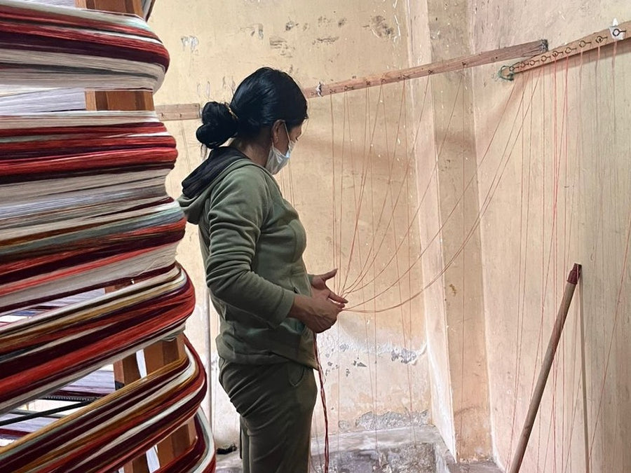 Una artesana amarra a mano los hilos en el urdidor de un taller de Peguche