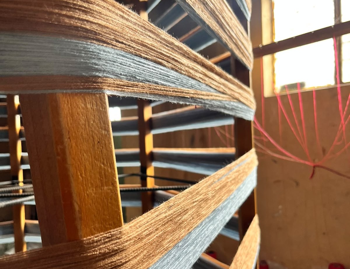 Hilos color cobre y gris claro enrollados en el urdidor de madera de un taller de Peguche